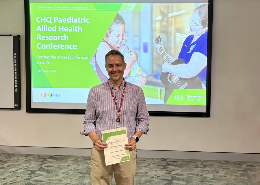 Tristan holding a Highly Commended certificate in front of a slide for the Children's Health Queensland Paediatric Allied Health Research Conference, 18 November 2025.