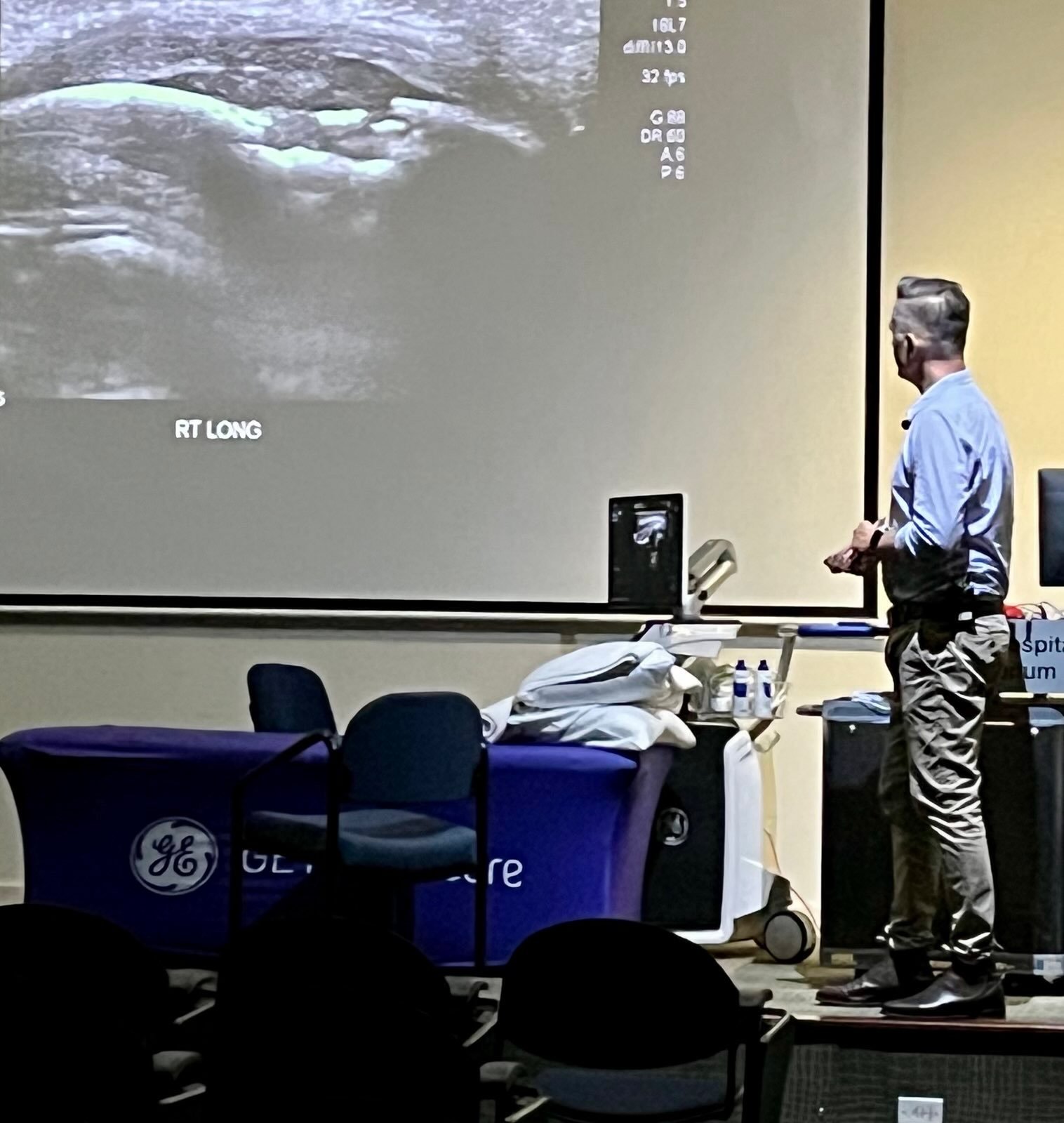 Tristan standing beside a projected ultrasound image of a hip during a regional workshop.