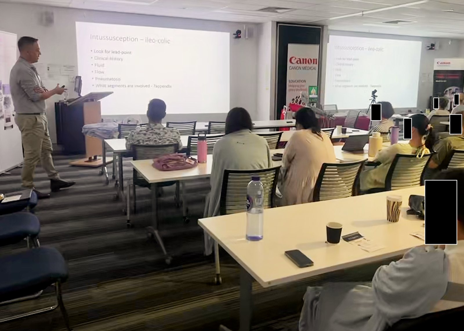 Tristan presenting a slide on intussusception to a seated audience in a training room. Faces in the audience are covered.